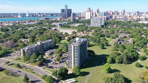 An aerial shot of an apartment building with greenery and city skyline in the background