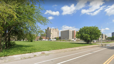 A vacant grassy lot in the foreground, with large buildings in the distance
