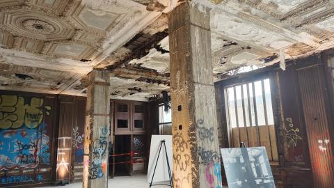 A large room with the ceiling falling apart and graffiti on the wall