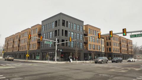 A brown and grey three-story apartment building on the corner of two streets