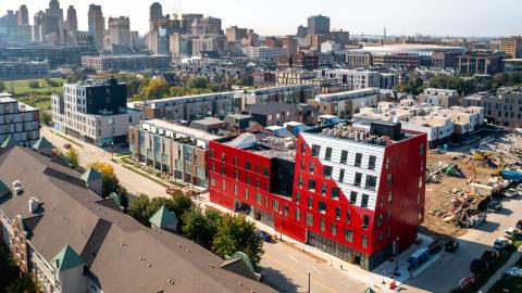 An aerial shot of a large read apartment building with condos next to it, and the Detroit skyline in the background