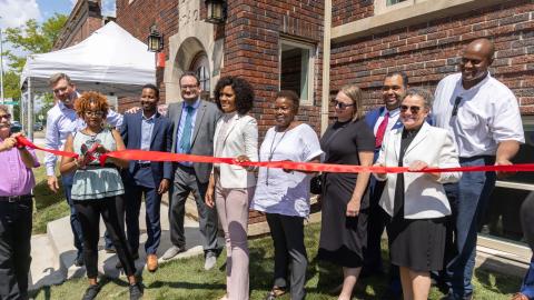 People stand in front of a brick building at a ribbon cutting