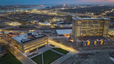 An overview of a 13-story train station next to a 4-story square building with a bridge in the background