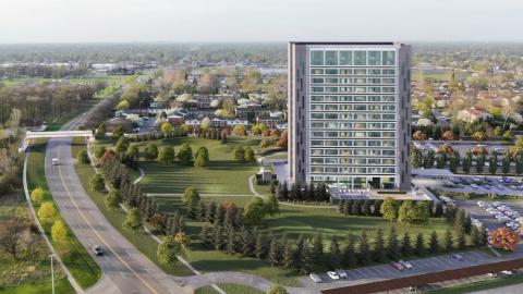 A high rise surrounded with a park next to a busy road