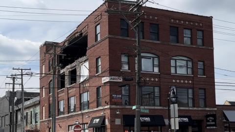 A four-story brick building with a large hole in the fourth and third floors