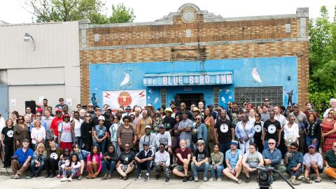 Many people in front of a small blue historic building